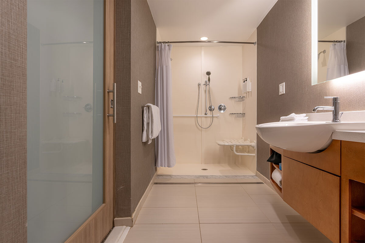 Salle de bains accessible avec douche de plain-pied équipée d'une barre d'appui et d'un rideau, meuble-vasque en bois