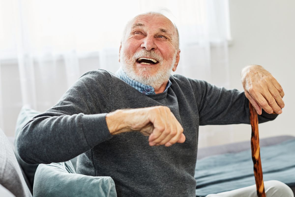 Homme senior riant avec sa canne de marche à la maison