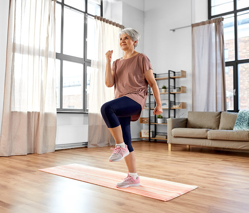 Femme senior souriante qui fait des exercices sur un tapis de sport dans un salon lumineux