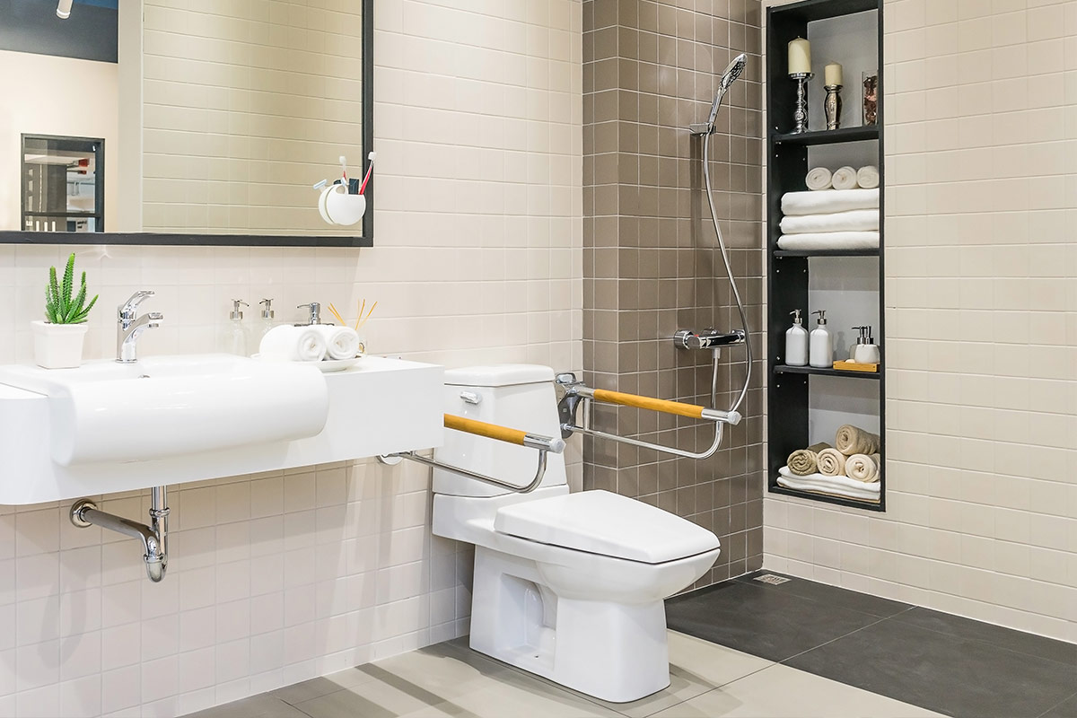 Salle de bain adaptée avec barres d'appui, siège de douche et douchette, dans un décor clair et moderne