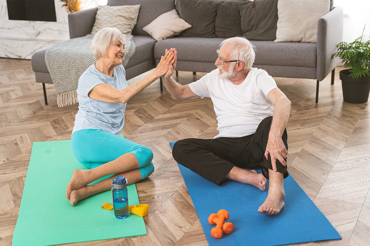  Couple de seniors qui se tapent dans la main après une séance de sport sur des tapis, dans leur salon