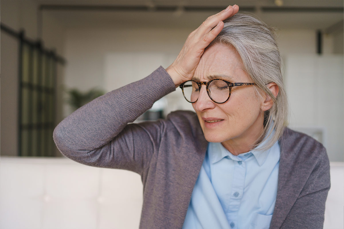 Femme senior à lunettes, la main sur le front et les yeux fermés, l'air soucieux